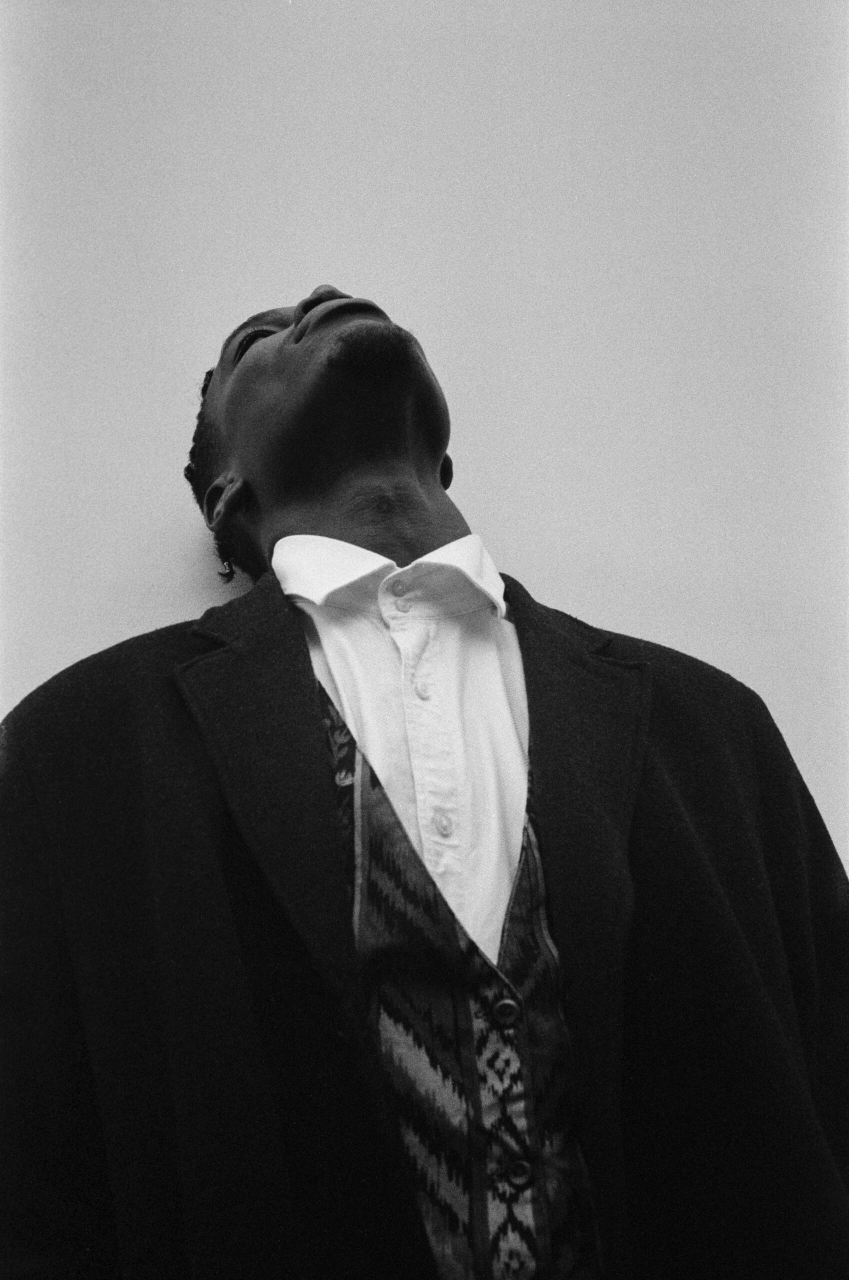 A black man in a suit leaning head back against a wall.